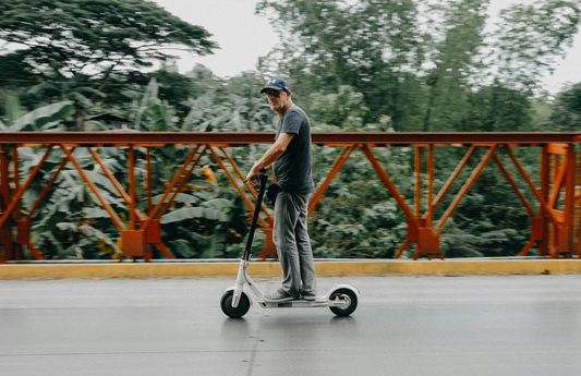 Mann fährt E-Scooter über eine rote Brücke mit grünem Dschungelhintergrund