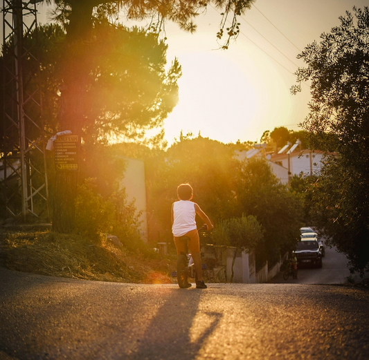 Kind fährt bei Sonnenuntergang Fahrrad durch Wohnstraße – goldene Lichtstimmung und ländliche Idylle.