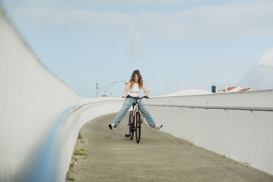 Eine junge Frau fährt mit ausgestreckten Beinen auf einem SUSHI BIKE über eine leicht gebogene Brücke