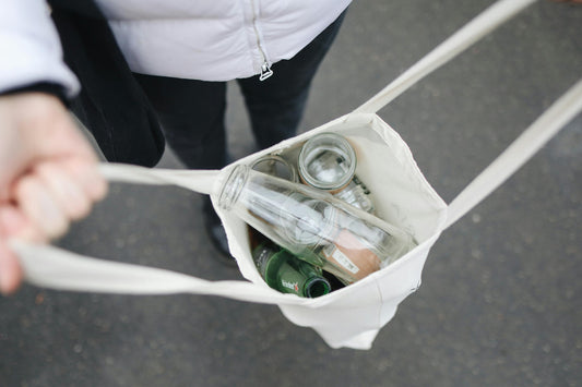 Eine Person trägt eine Stofftasche voller leerer Glasflaschen – unterwegs zum Recycling und dabei bewusst nachhaltig handeln.