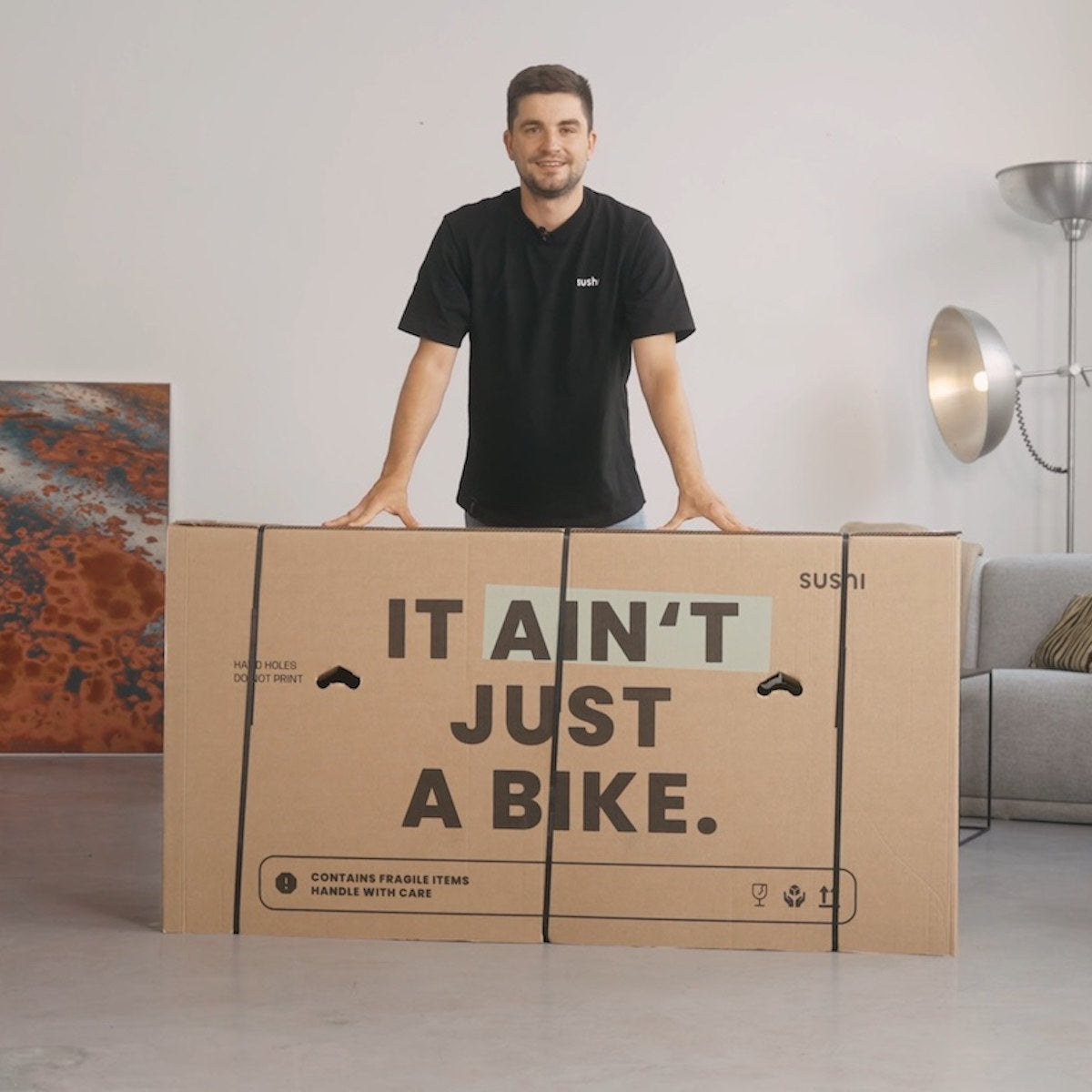 Mann steht hinter einem SUSHI BIKES Karton, in dem das E-Bike verpackt ist