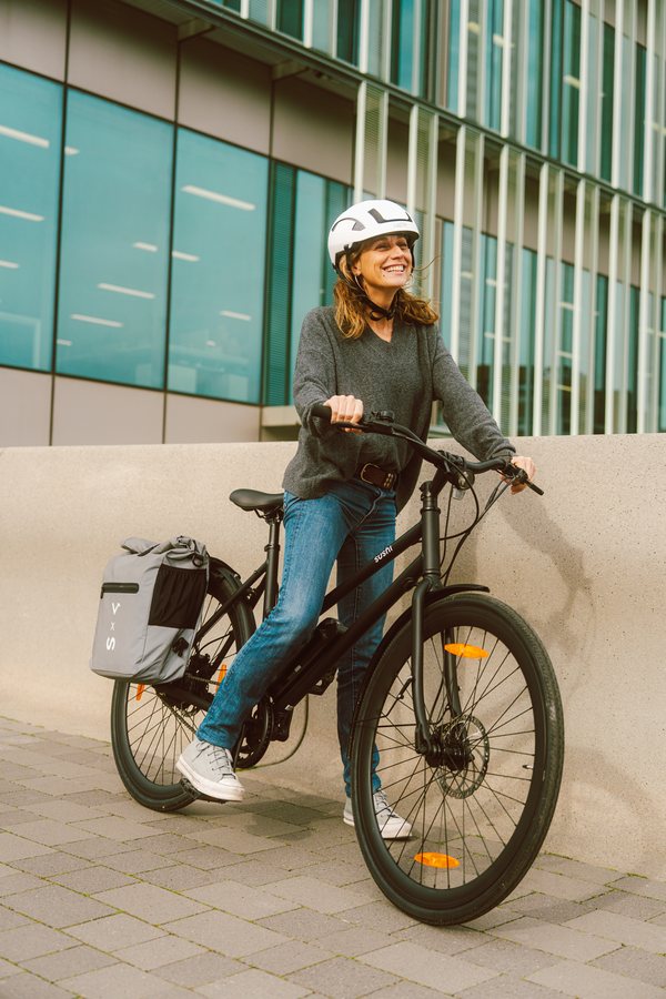 Frau mit Helm auf schwarzem E-Bike von SUSHI BIKES mit Gepäcktasche am Schutzblech befestigt
