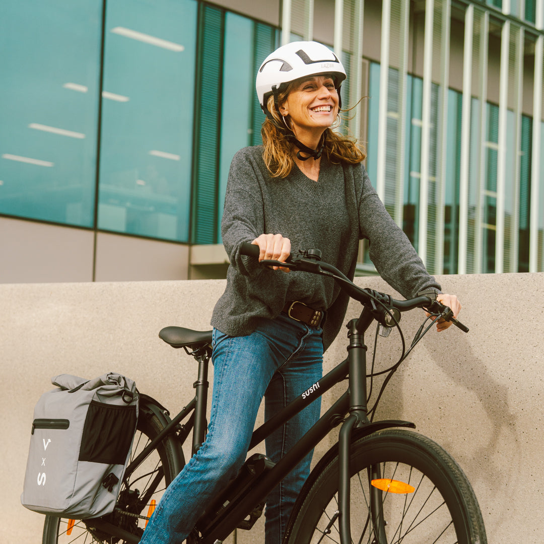 Frau mit Helm steht lächelnd mit einem schwarzen E-Bike von SUSHI BIKES