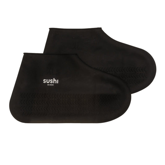 Schwarze SUSHI BIKES Schuhüberzieher aus Silikon seitlich fotografiert mit weißem SUSHI BIKES Logo