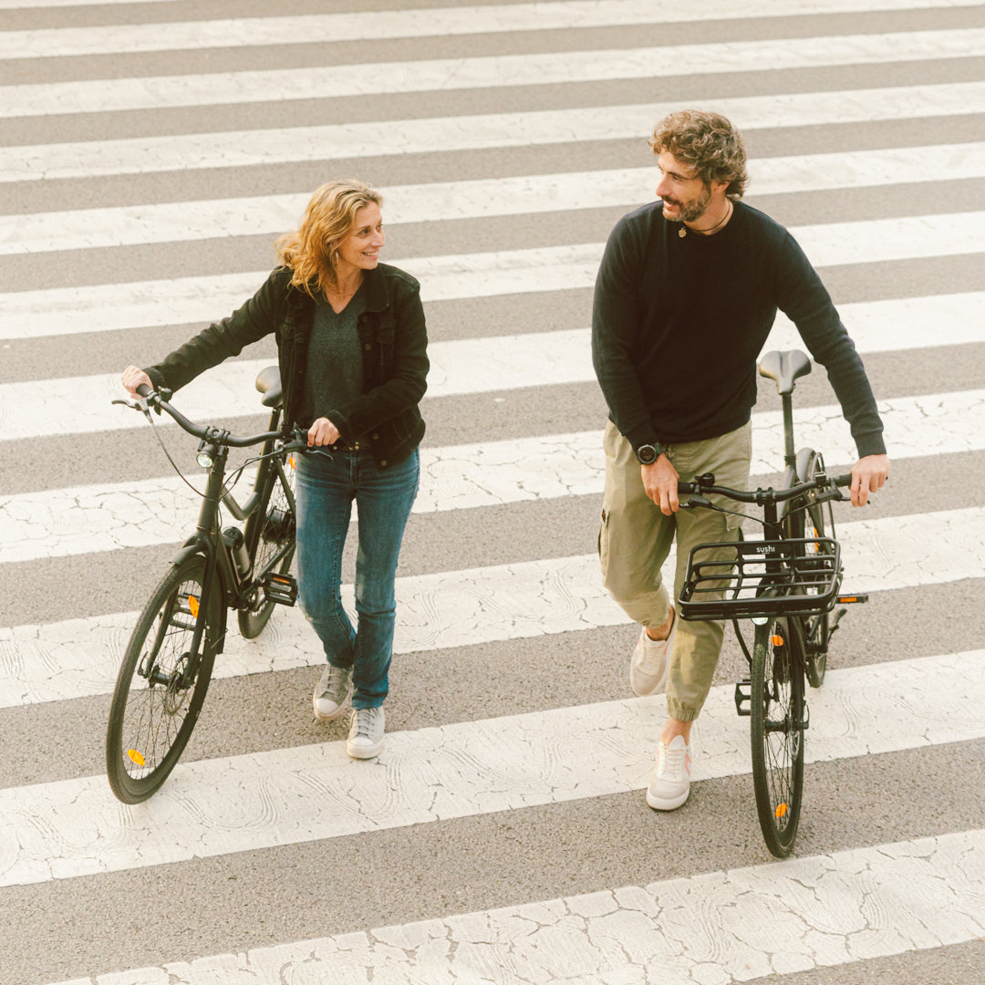 Eine Frau und ein Mann schieben zwei E-Bikes von SUSHI BIKES auf einer Straße