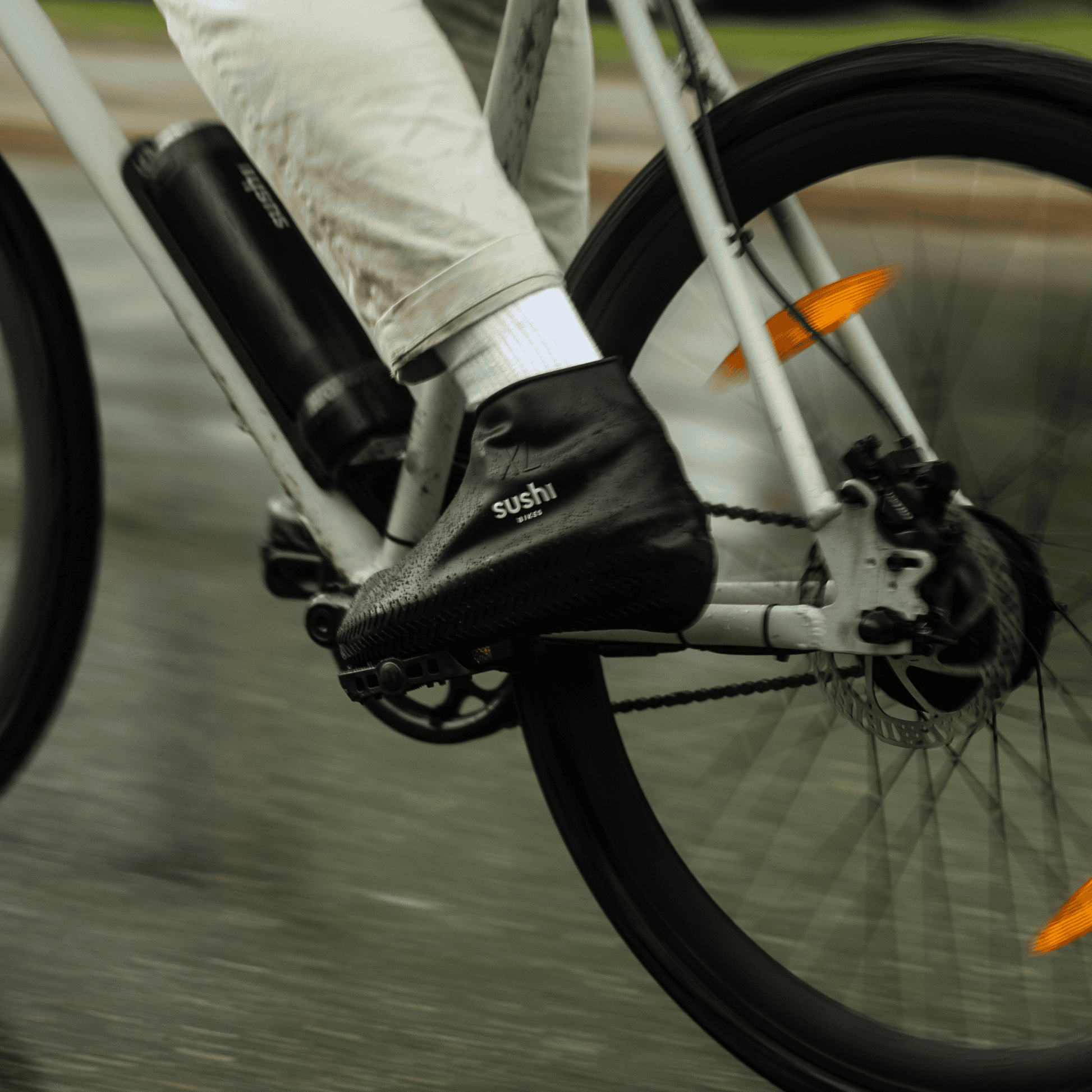 Person trägt SUSHI Schuhüberzieher beim Fahrradfahren auf nassem Asphalt