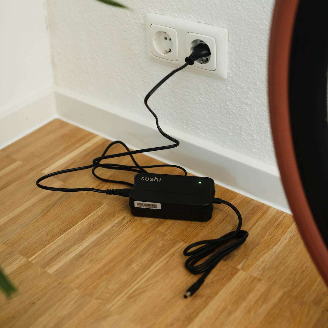 SUSHI BIKES Speed Charger mit grün leuchtender LED angeschlossen an einer weißen Wandsteckdose