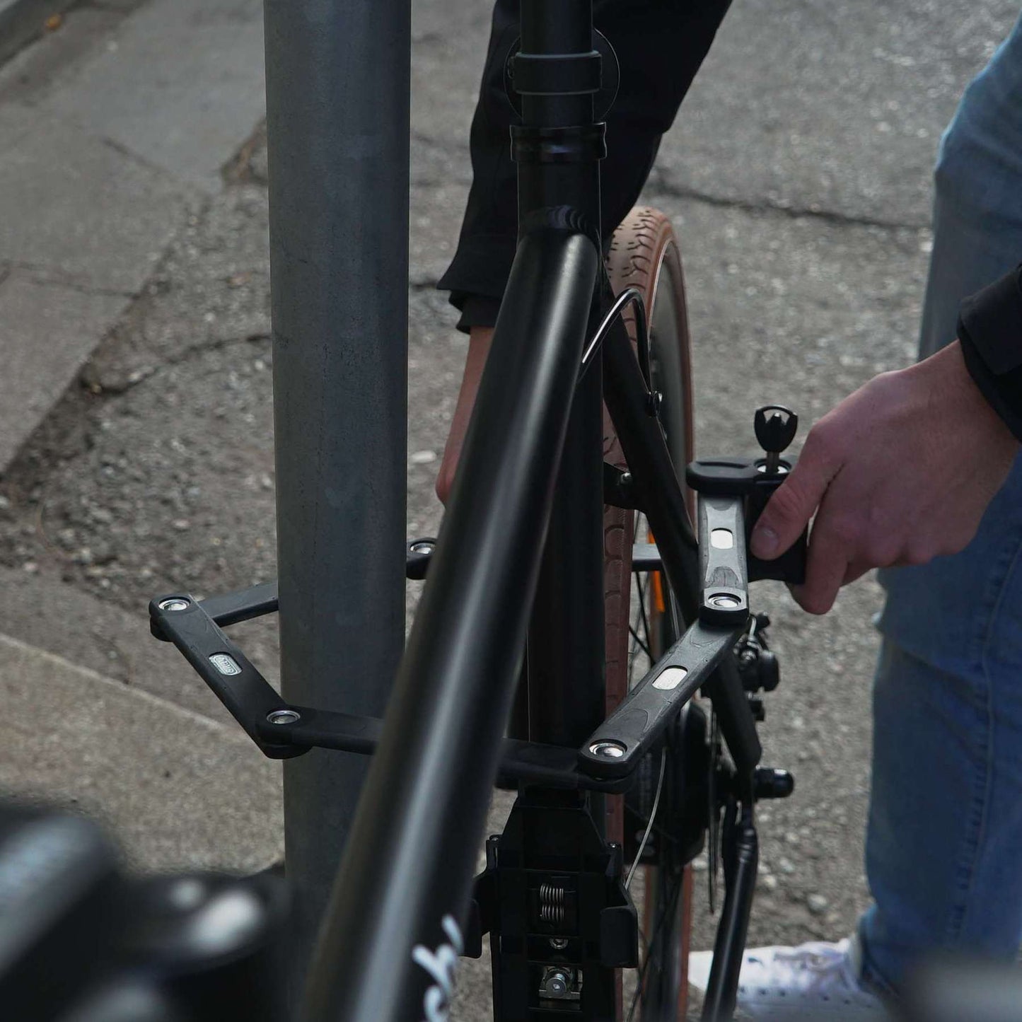 ABUS-Faltschloss wird um Sattelrohr und Laternenpfahl gelegt, sichert das schwarze Fahrrad gegen Diebstahl