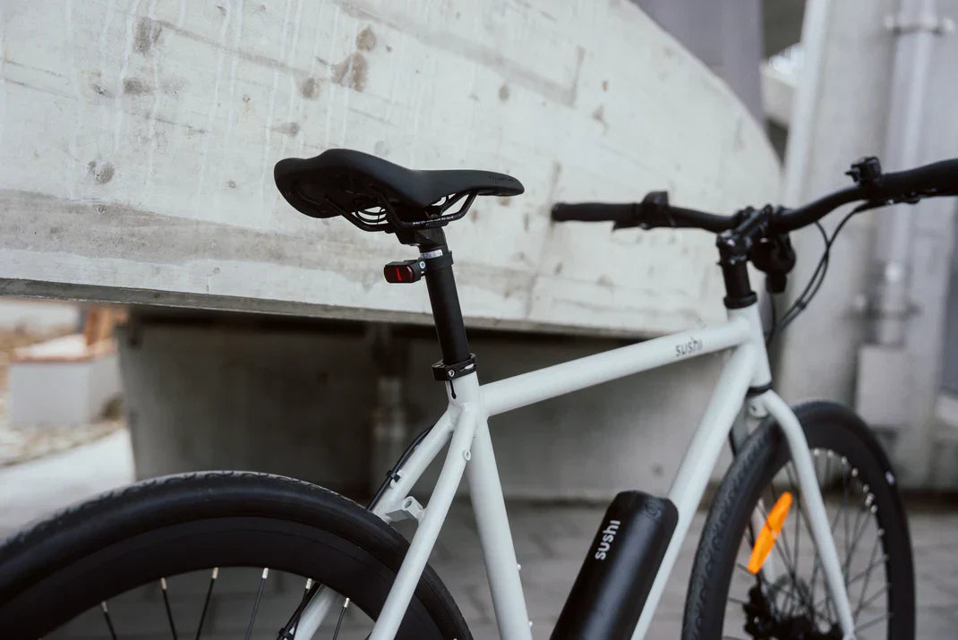 Modernes weißes E-Bike mit schwarzem Akku und cleanem Rahmen-Design vor urbanem Betonhintergrund.