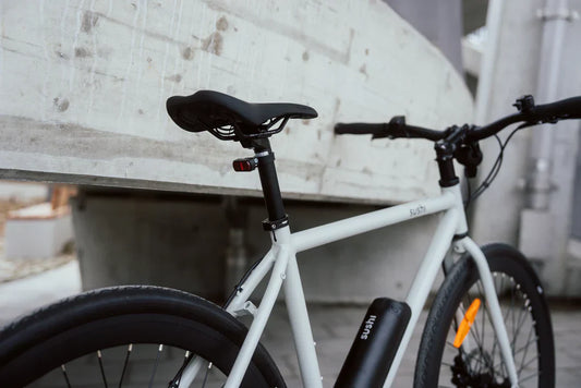 Modernes weißes E-Bike mit schwarzem Akku und cleanem Rahmen-Design vor urbanem Betonhintergrund.
