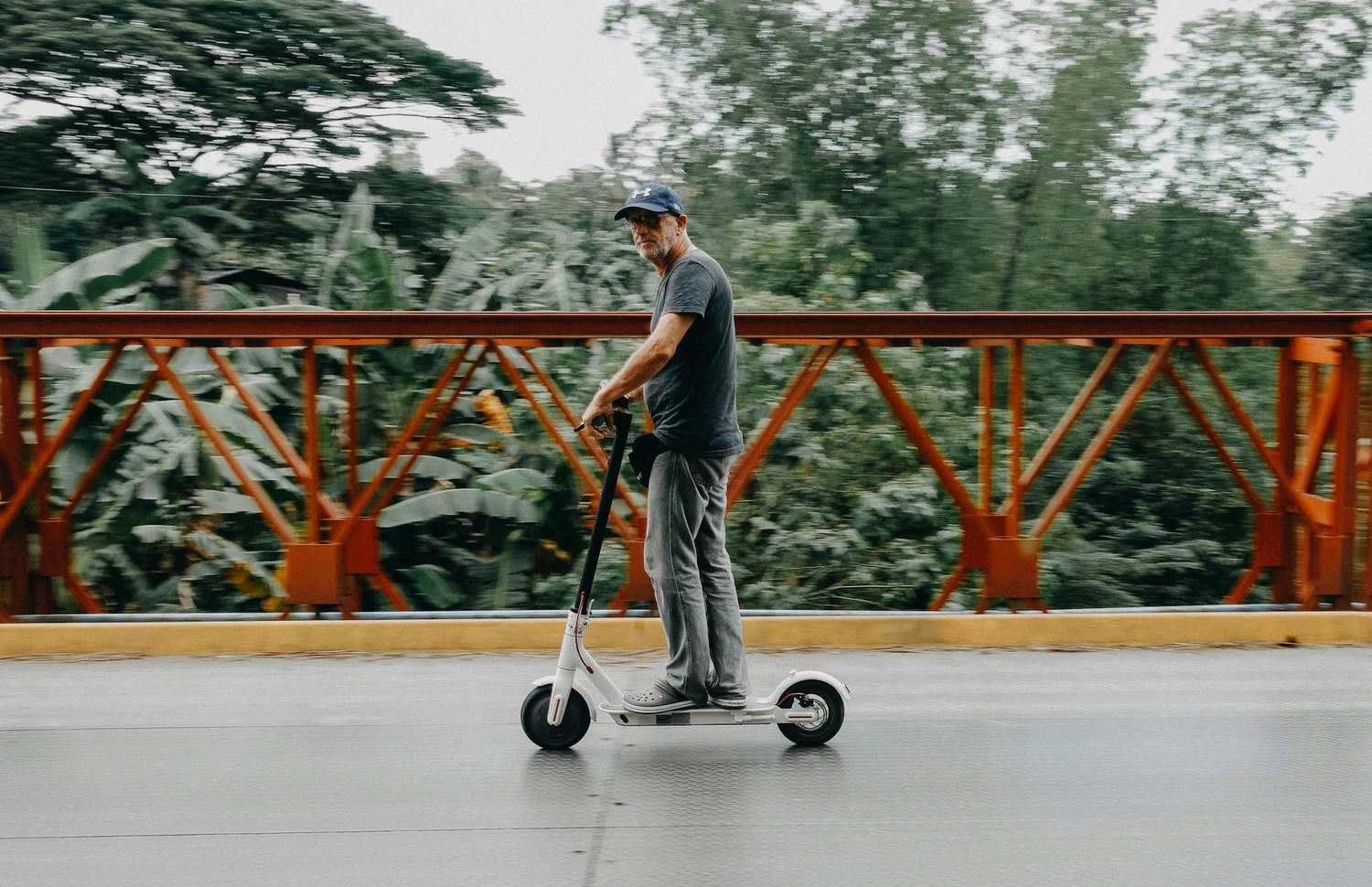 Mann fährt E-Scooter über eine rote Brücke mit grünem Dschungelhintergrund