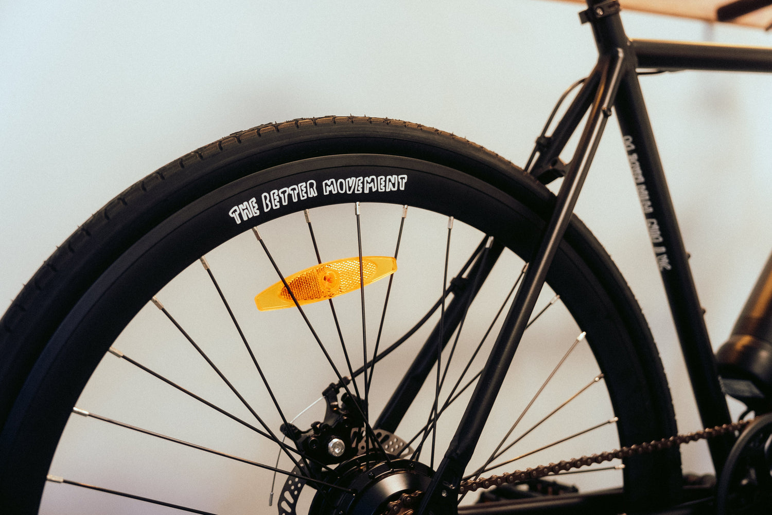 Die Nahaufnahme zeigt das Hinterrad eines schwarzen SUSHI BIKES E-Bikes mit dem weißen Schriftzug „THE BETTER MOVEMENT“ auf dem Reifen.