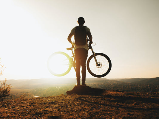 Mann steht mit Fahrrad beim Sonnenuntergang auf dem Berg
