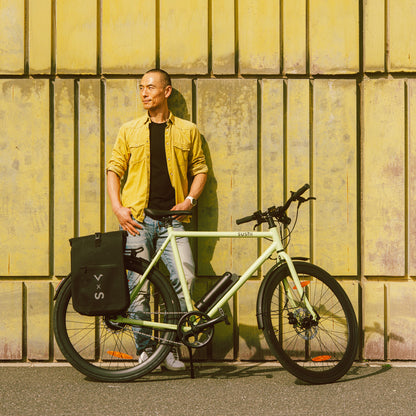 Maki 3.0+ Matcha, Mann steht mit E-Bike und Fahrradtasche vor einer gelben Wand