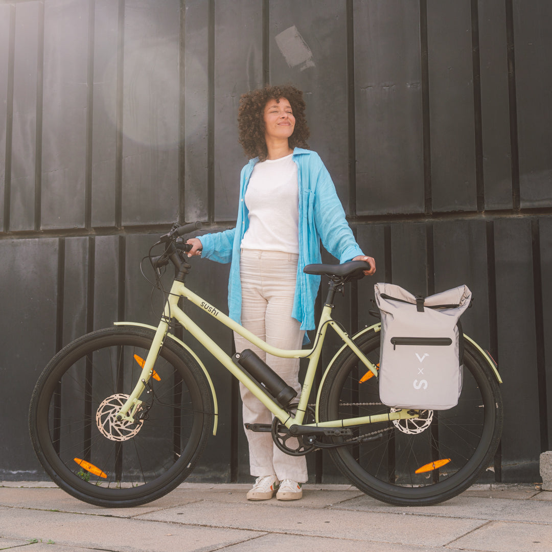 Frau steht neben einem matchafarbenen E-Bike von SUSHI BIKE mit grauer Gepäcktasche