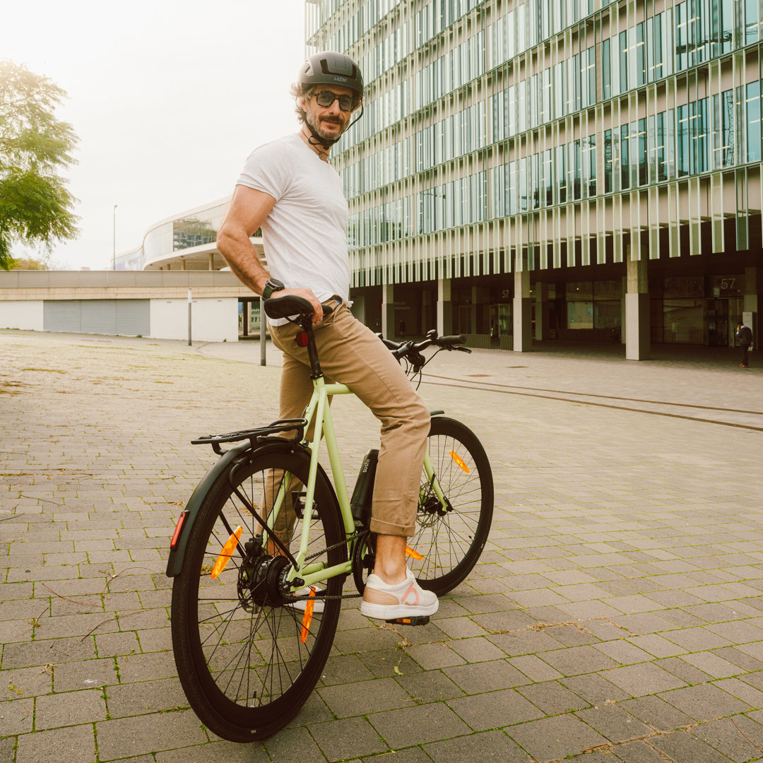 Mann mit schwarzem Helm auf SUSHI BIKES E-Bike Maki 3.0+ in Matcha vor modernem Bürogebäude